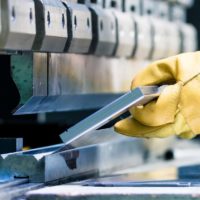 Image of gloved hands holding a piece of metal on a pressbrake